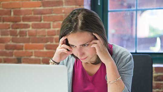 Woman holds her head while looking at her computer screen